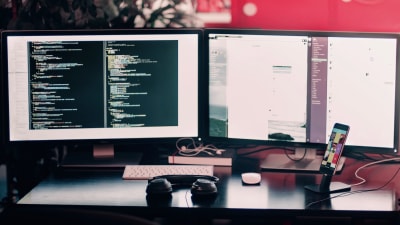 Coding work on a dual-monitor setup on a desk with headphones and cell phone.